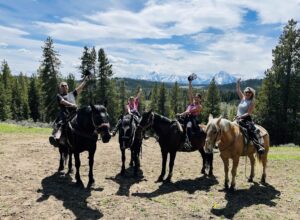 A little family of four enjoying their view of the Tetons on horseback by having their hands in the air of excitement.